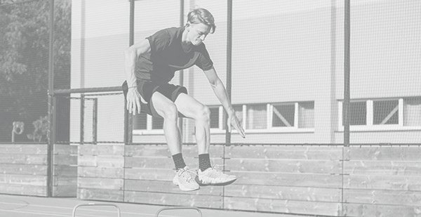 Blond boy in sportswear jumps over red obstacles to improve lower body dynamics. Plyometric training in an outdoor environment. Improve your skills